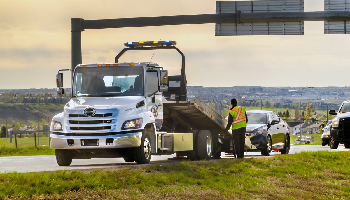 Roadside technician assisting a driver with a broken-down car on the highway shoulder